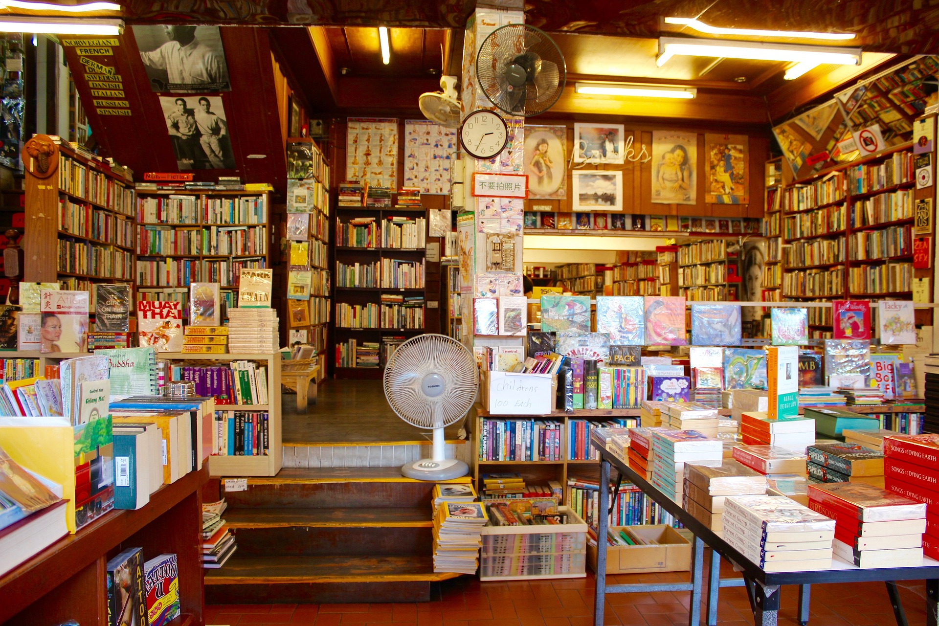 Book store with books on tables and shelves, wall-to-wall throughout the room.