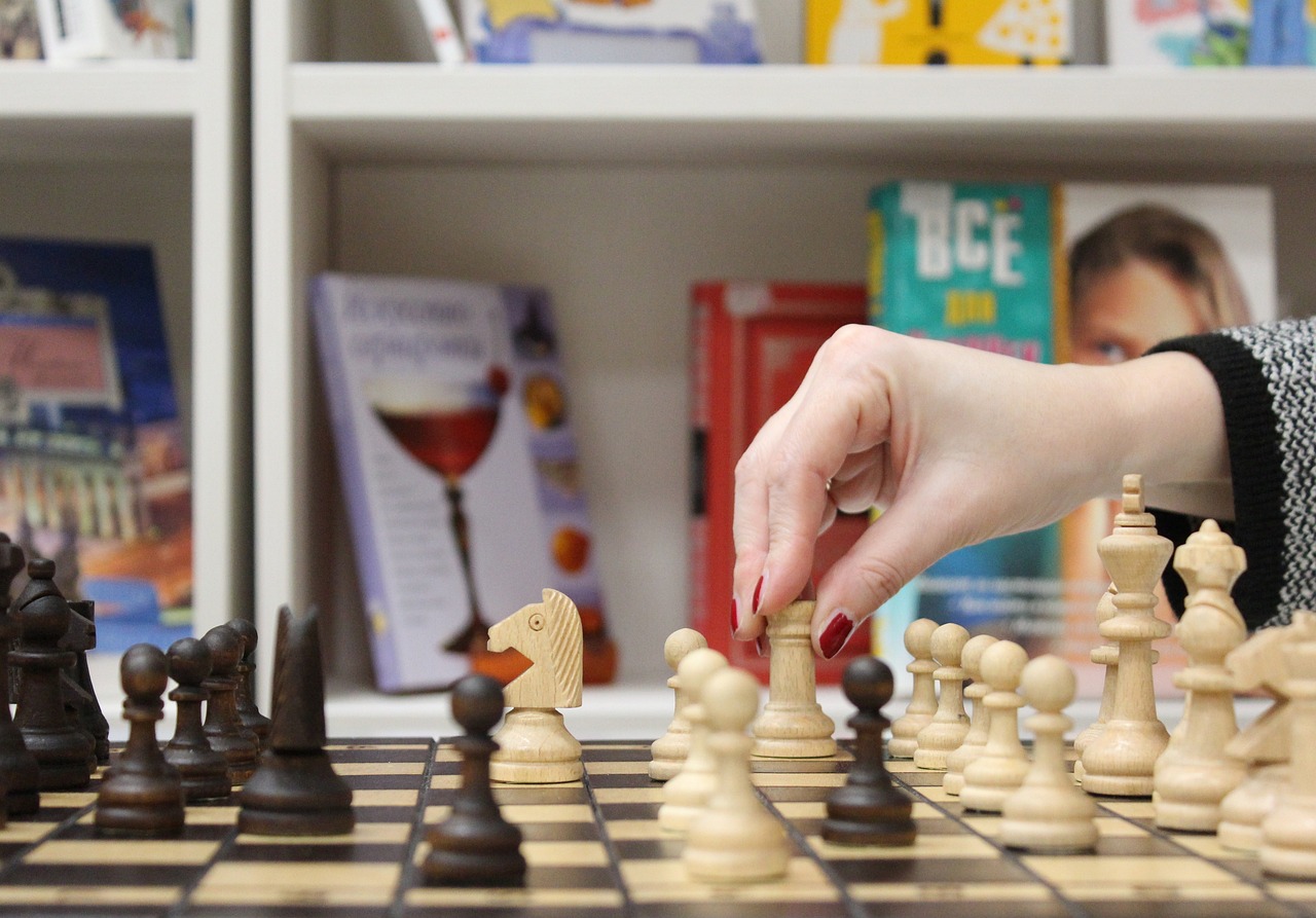 Hand with chess piece over a chess board with children books in the background