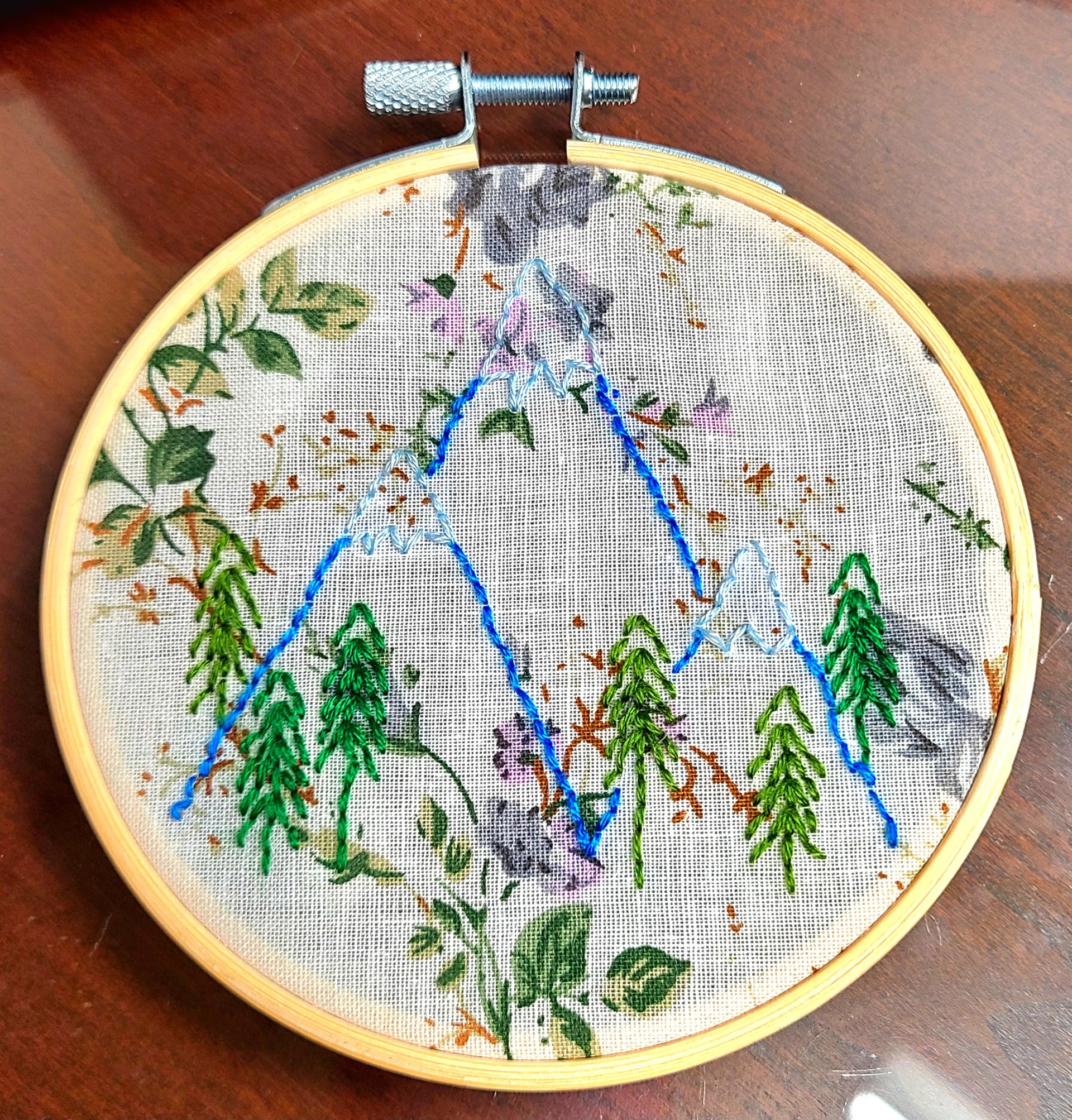 Embroidery hoop with three mountains and some trees in the center