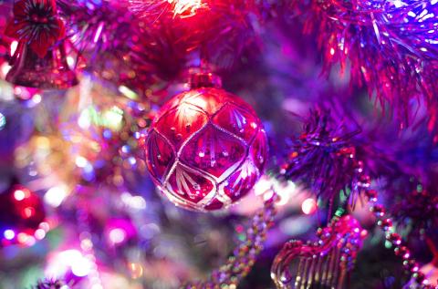 Pink round ornament hanging on a Christmas tree with twinkling colored lights