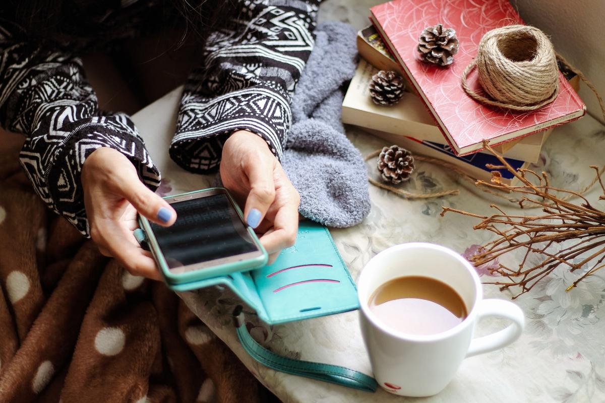 Women holding phone with coffee and a book stack next to her