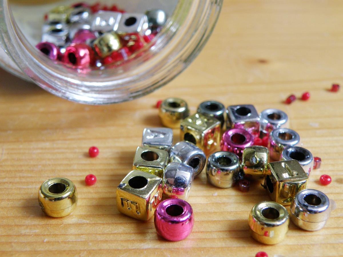 Pink, silver, and gold beads scattered outside of a jar on a table